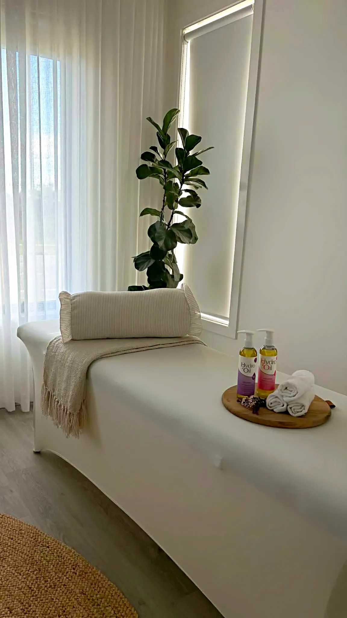 The treatment bed made up with a bolster and folded towels, beside a bright window and a potted plant